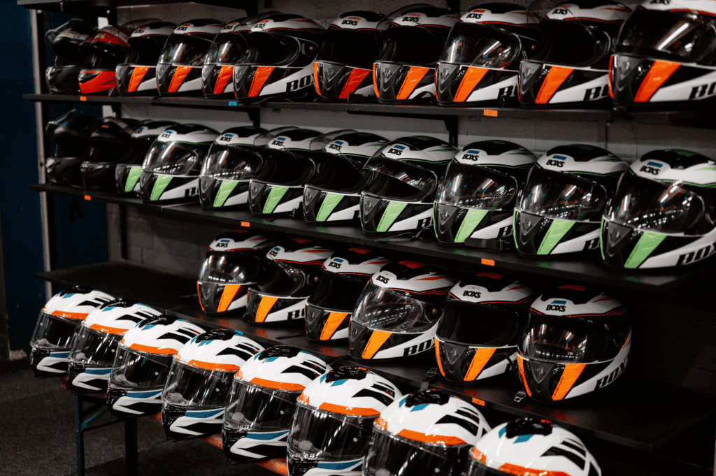 Bunte Schutzhelme in verschiedenen Größen ordentlich im Regal im Kartcenter Cologne für sicheres Kartfahren Köln.