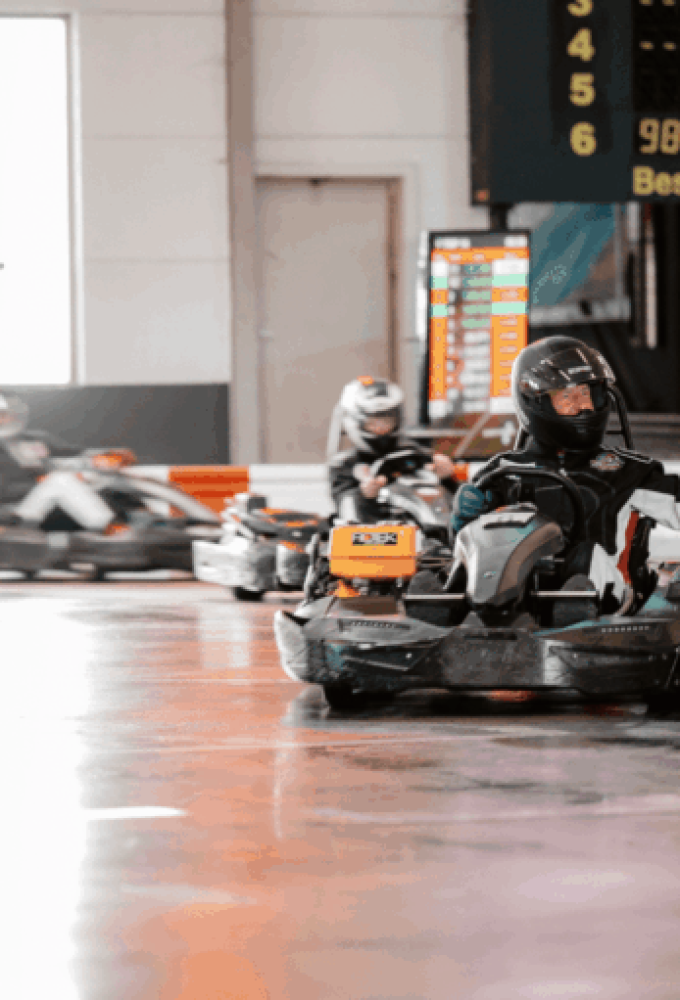 Drei Karts fahren hintereinander auf der Strecke des Kartcenter Cologne, der vordere Fahrer winkt beim Kartfahren Köln.